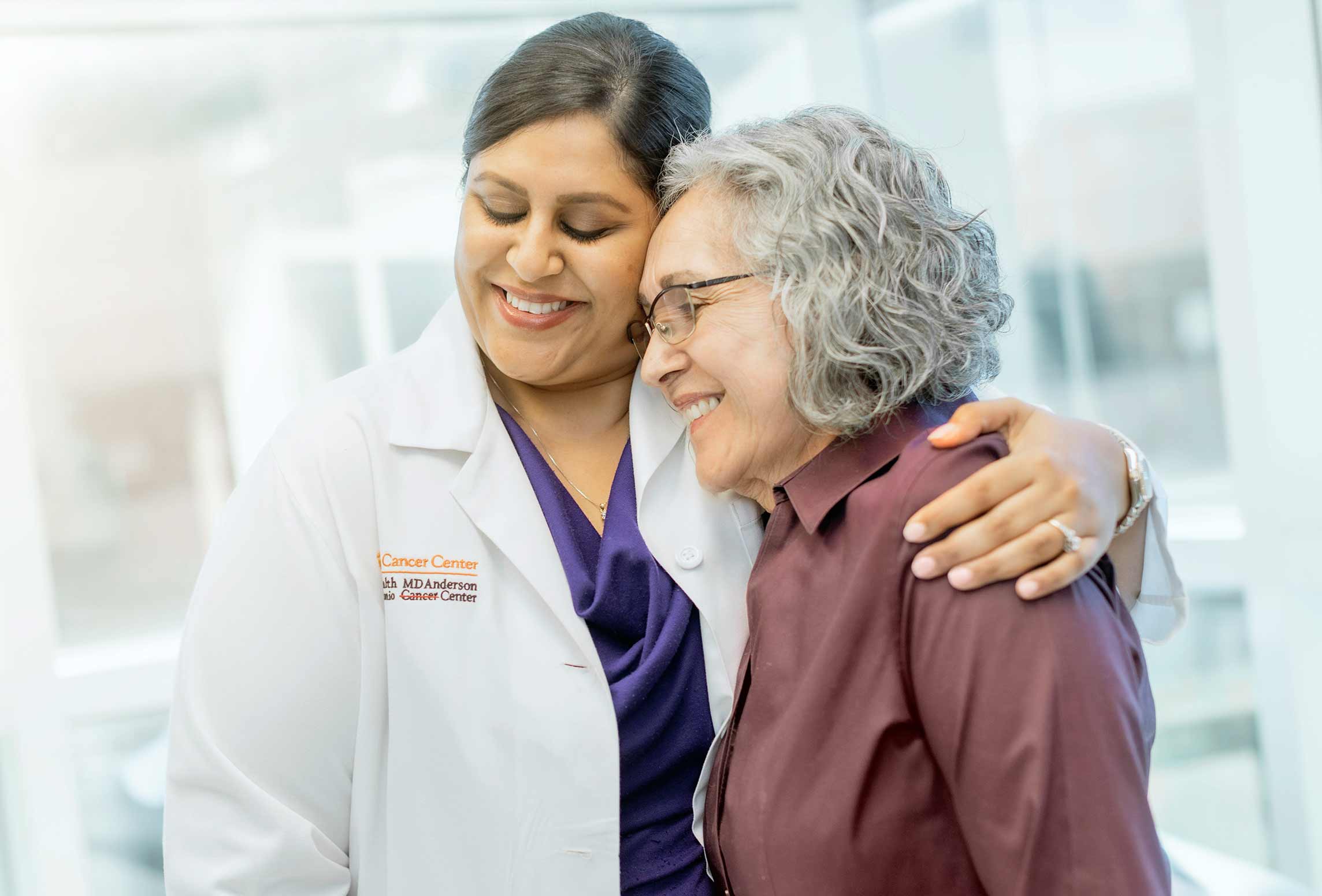 Female doctor smiling and hugging senior female patient