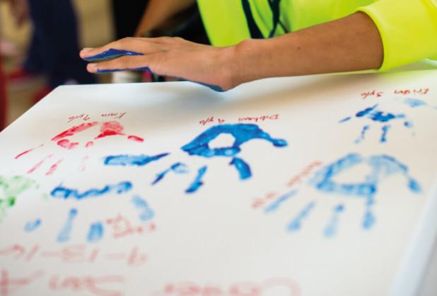 A child prepares to press their painted alongside other handprints.