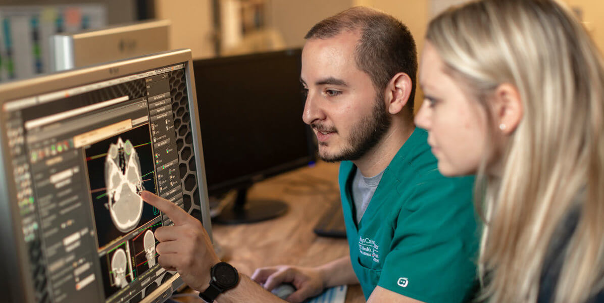 A man in teal scrubs and a woman looking at a brain scan on a computer