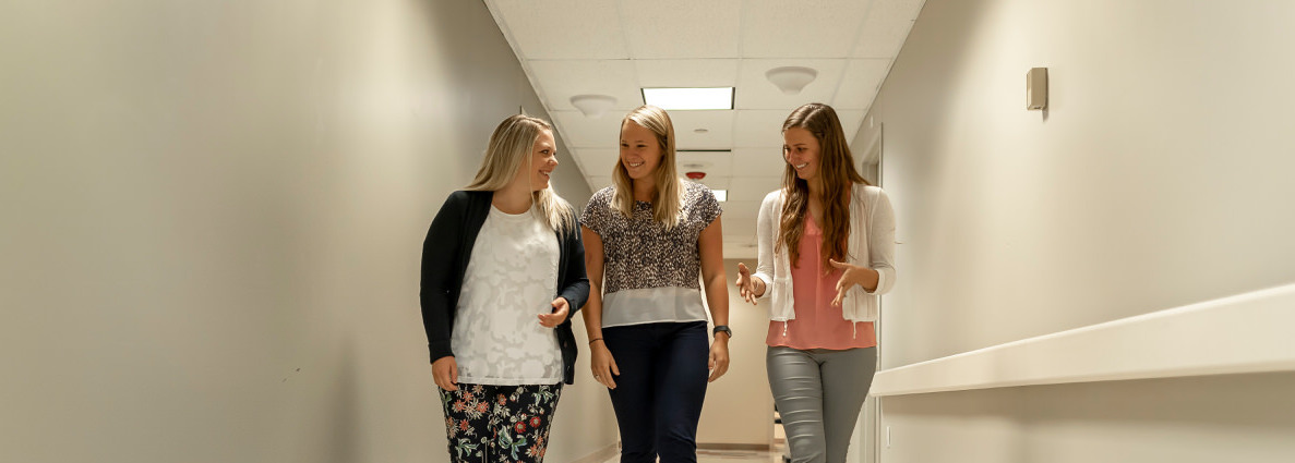 Three girls walking down a hallway talking and smiling.