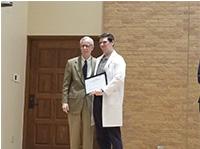 A man in a suit and a man in a white coat holding a certificate and posing for the camera.