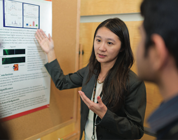 Student presenting research poster to others