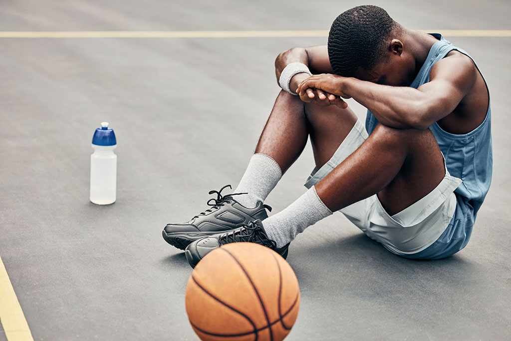 A basketball player on the ground with his head resting in his lap.