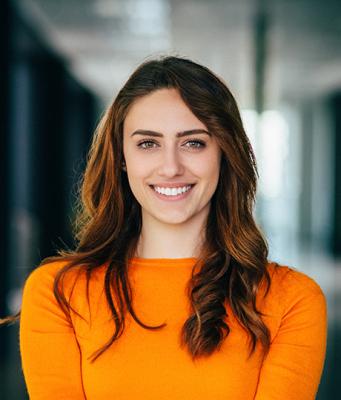 A young woman smiling, wearing an orange sweater