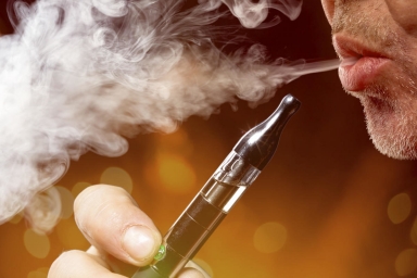 A close-up portrait of a man smoking an e-cigarette; smoking is a significant part of the current triple threat to lungs.